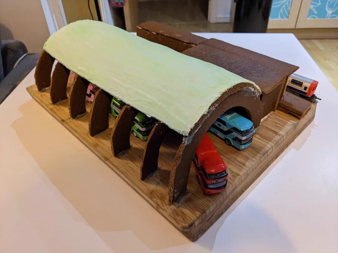 A gingerbread Newbury Park station with model buses and a train.