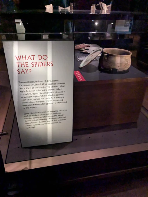 Display from the 'Oracles, Omens an Answers' exhibition. The information board explains that 'the most popular form of divination in Cameroon in Central Africa involves tarantula-like spiders or land-crabs. The spiders, called ngámbi, live in holes in the ground. When consulting, ngám diviners place a stick and a stone near a spider's hole, which is covered with some marked leaf cards. As it emerges from its hole, the spider moves everything around and the resulting pattern is interpreted by the diviner.'