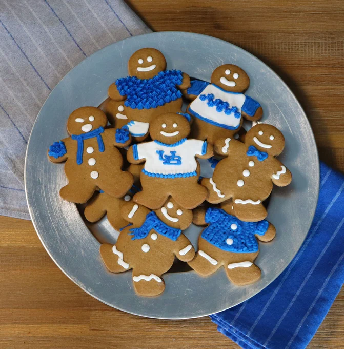 A plate of gingerbread cookies decorated with blue and white icing. The gingerbread in the middle is wearing a "sweater" with the interlocking UB logo on it.