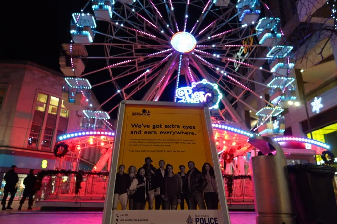 Christmas Ferris wheel can be seen lit up on The Moor in Sheffield with a Project Servator a-board in the fore. The a-board states 'we've got extra eyes and ears everywhere.