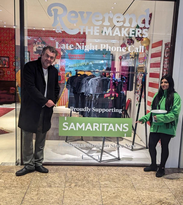 A photo of Jon from reverend and the makers and a Samaritans volunteer in front of Revered and the makers pop up shop. 