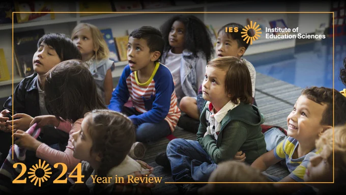 Young students displaying a variety of emotions sit on the floor and look up at a teacher 
