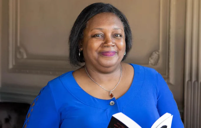 Author Malorie Blackman OBE smiles and holds an open book