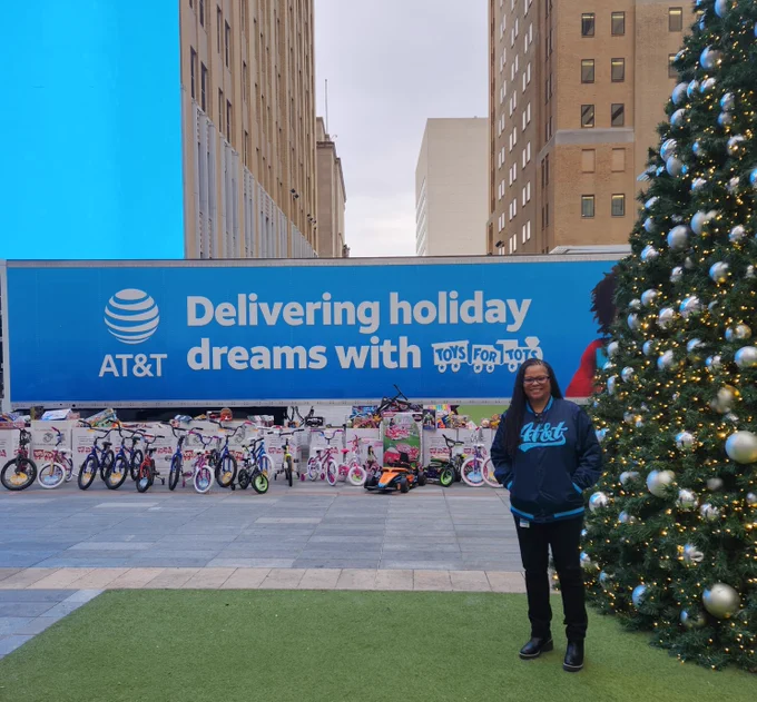 Keysha in front of Toys for Tots truck. It's blue with the AT&T logo and says "Delivering holiday dreams with Toys for Tots"
