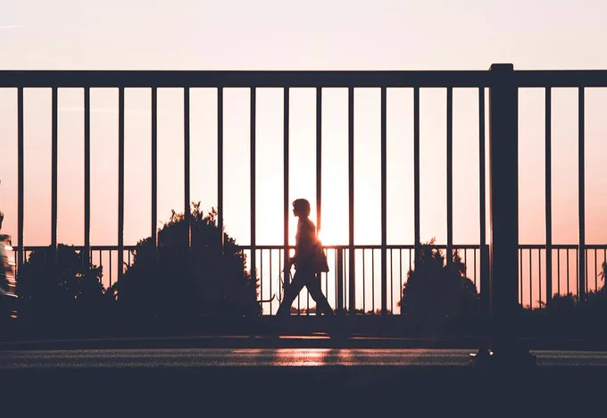 Photo of a man walking down a street, he is silhouetted by the sun behind him. Photo by Kasper Rasmussen on upsplash.