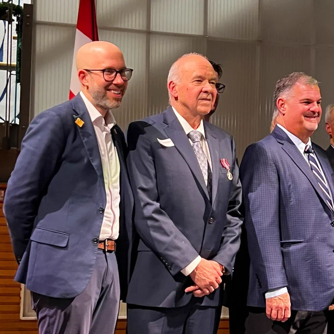 A photo of three men in suits standing together and posing for a photo.