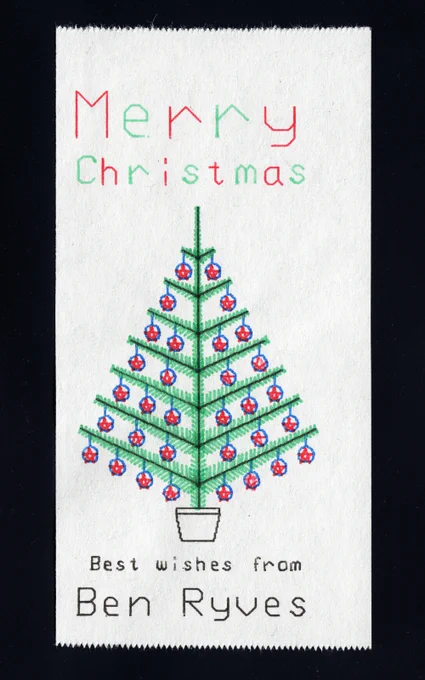 Scan of a printout of a crude colour drawing of a Christmas tree. The tree has blue baubles with red stars hanging on each branch, and there is writing that says "Merry Christmas" in alternating red and green letters above the Christmas tree and "Best wishes from Ben Ryves" in black text underneath.