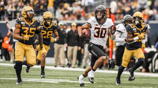 Chuba Hubbard carries the football while three defenders chase him during an Oklahoma State Cowboys football game against the West Virginia Mountaineers.
