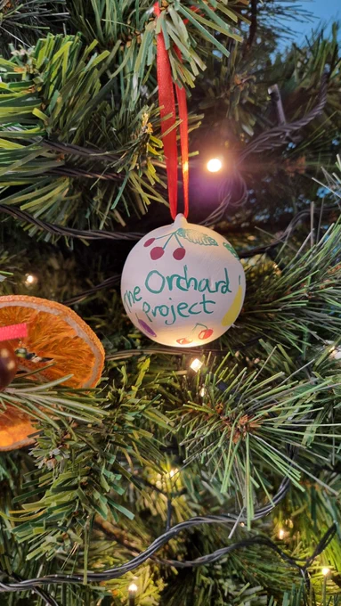 Christmas bauble with The Orchard Project written on, hanging on a tree by a red ribbon