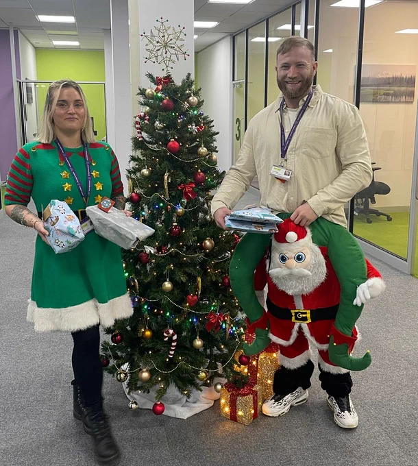 wo council officers in festive outfits holding several wrapped presents.