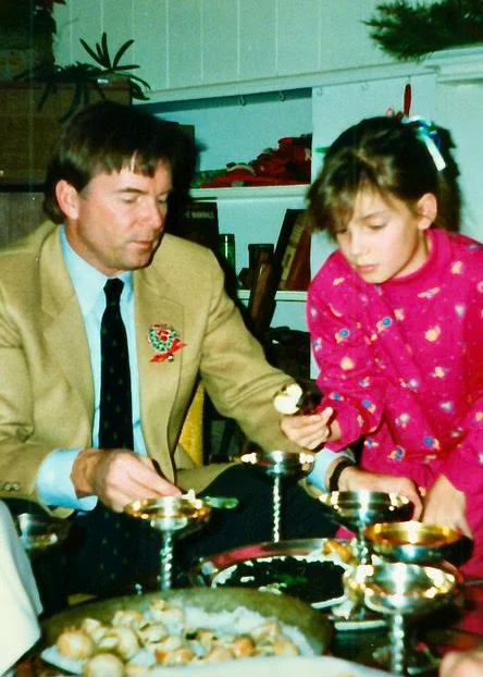 A man in a beige suit and a young girl in a bright pink sweater serve themselves caviar and escargot around the coffee table.