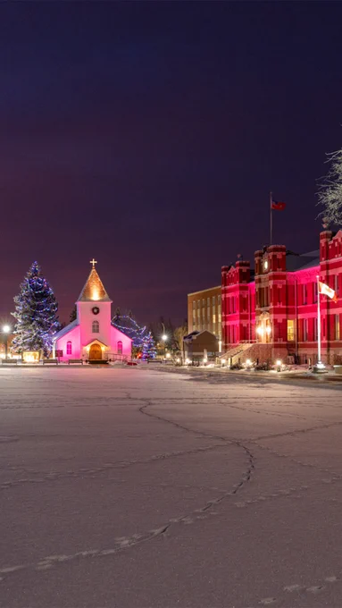A brick building and chapel on a snowy day with red lights shining.