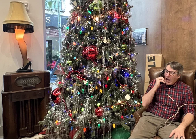 Brandon is seated in front of makeshift set from the film A Christmas Story, yelling into an old fashioned rotary phone.