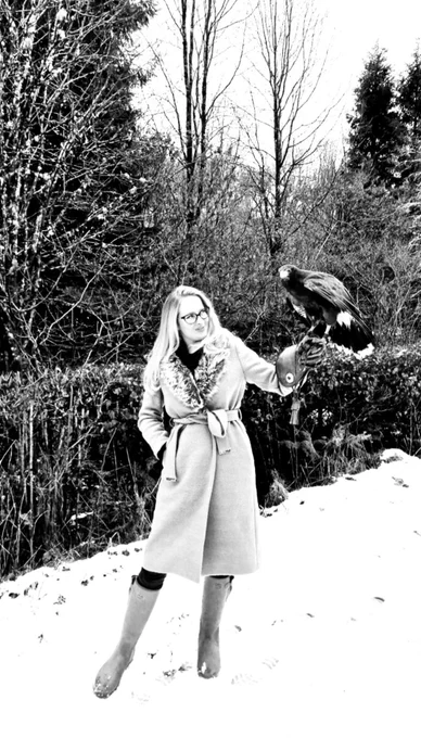 Tory stands in the snow admiring a harris hawk perched on her arm