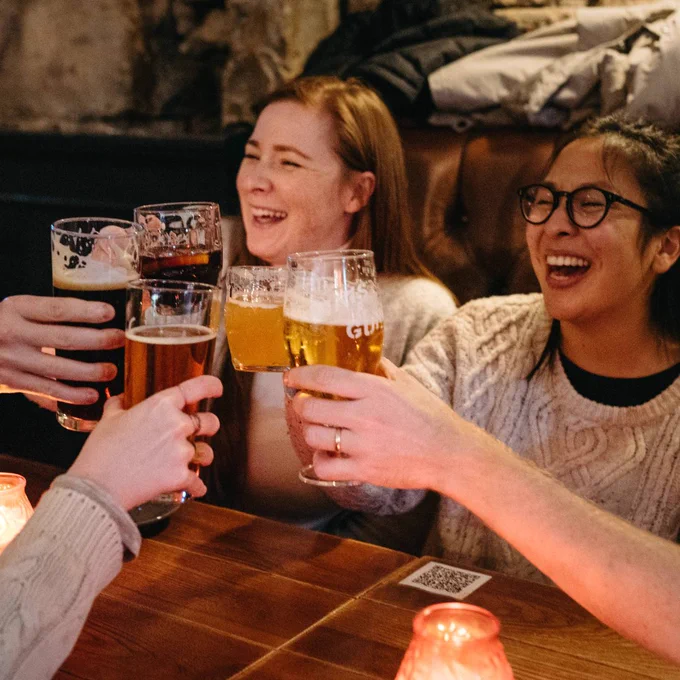 A group of young people laughing and cheering their pints of beer