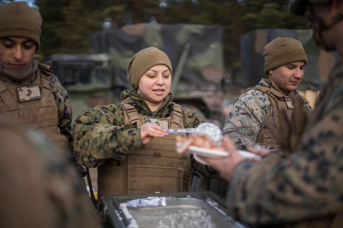 A Marine Corps Reservist in cold-weather gear serves a meal to fellow Marines from a field kitchen setup during a training exercise. (U.S. Marine Corps photo by Cpl. Niles Lee)
