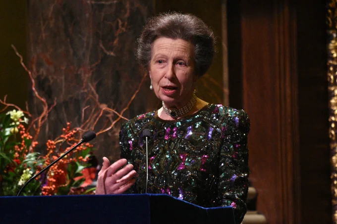 HRH The Princess Royal speaking on a stage, behind a microphone with flowers in the background.