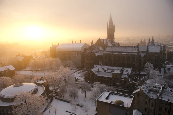 Beaming sunlight seen across a skyline. The University of Glasgow Gilmorehill campus buildings are topped with a blanket of snow.