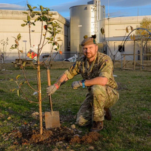 A uniformed Reservist holding a shovel while planting a tree.