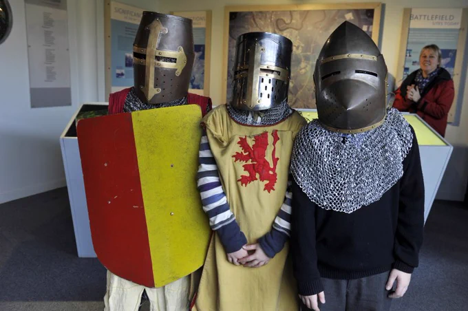 Three children dressed up as knights wearing helmets. 
