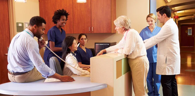 A group of health care professionals converse around a desk in a hospital setting