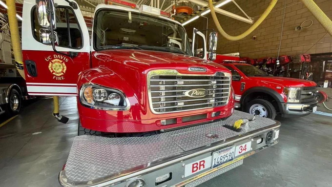 The front of a UC Davis fire engine with it's doors open. It's parked next to another UC Davis Fire vehicle in a garage. 