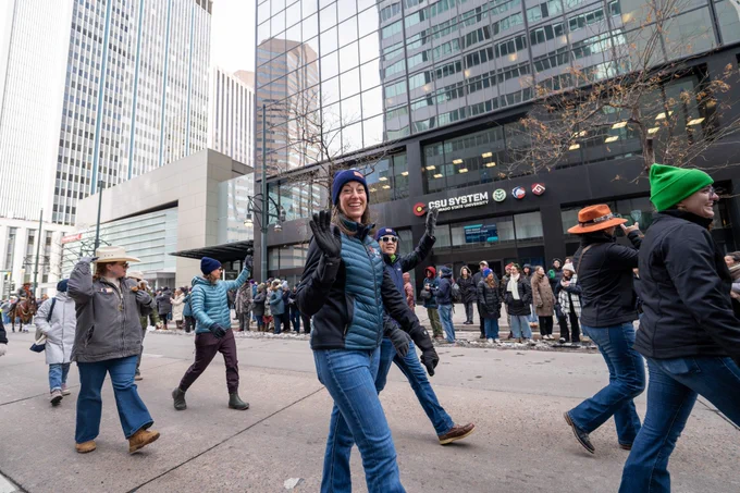 A group of people walking in a parade group down 17th street in Denver in front of the CSU System office