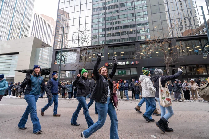 A group of people walking in a parade group down 17th street in Denver in front of the CSU System office