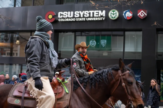 Two people on horses in a parade group walking down 17th street in Denver in front of the CSU System office