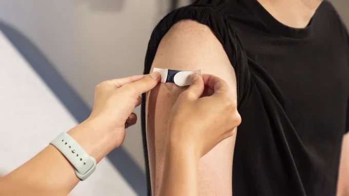 A person applying a bandage on another person's upper arm.