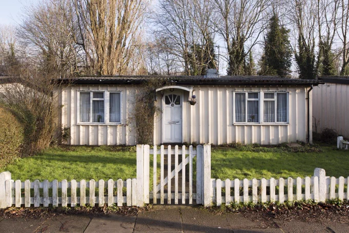 A photograph of a cream prefab house with a white wooden fence leading to it.