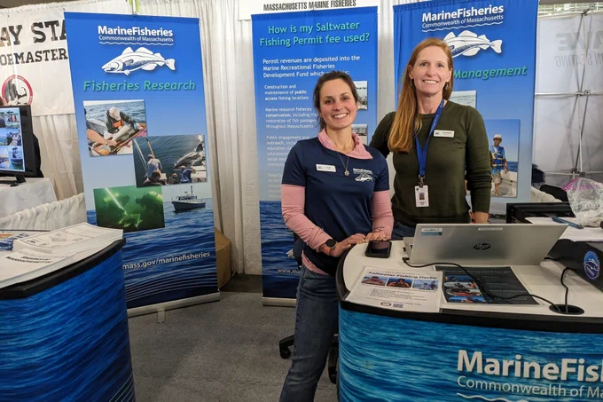 Two smiling staff members at the Division of Marine Fisheries booth during the 2025 New England Boat Show.