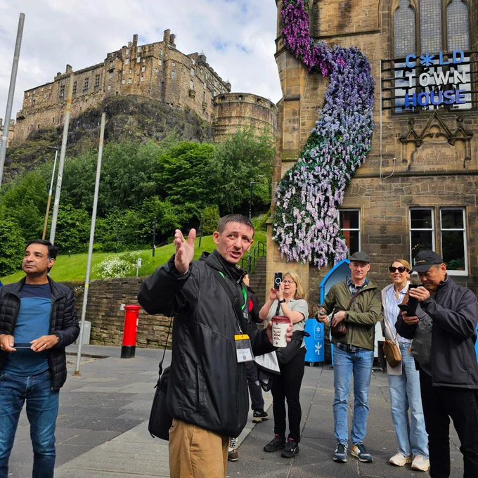 A tour guide from Invisible Cities points to something of interest out of shot for tourists to look at. Edinburgh Castle is in the background.