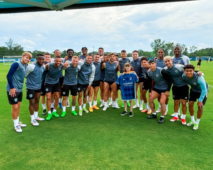Group photo of  Sporting KC players with a young fan on the soccer field.