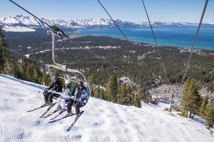 A group of three people are in a ski lift above snow in Lake Tahoe.