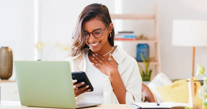 An excited young woman wearing glasses reading news on mobile device