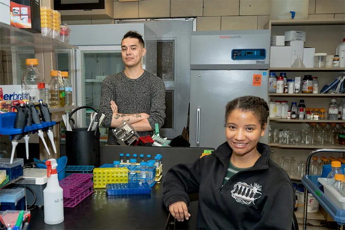 Joseph Peterman and Yeritmary Rodriguez Delgado, two participants in the Postbac Research Fellowship in Quantitative Biology, are in a lab, smiling at the camera.