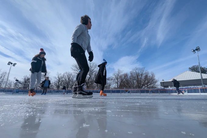 Skaters glide across an ice rink under a clear blue sky.