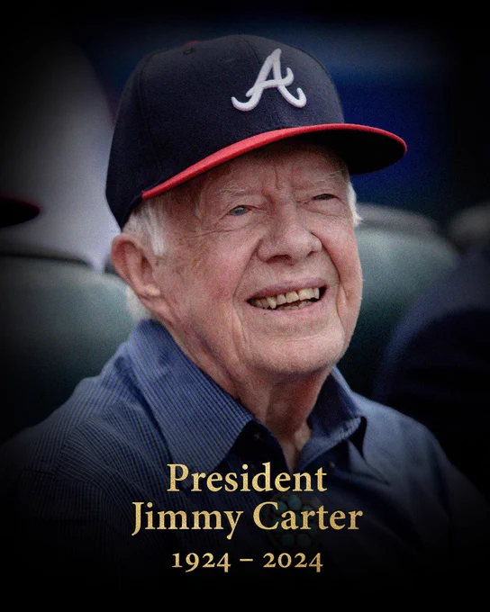 A picture of Jimmy Carter smiling in the stands at Truist Park while wearing a Braves hat. Caption: President Jimmy Carter. 1924-2024