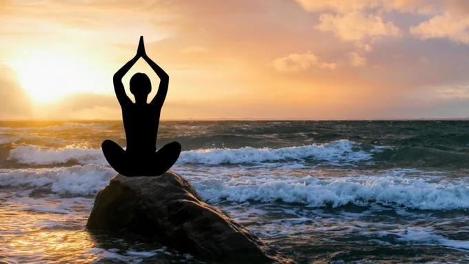 Back shot of woman facing sunrise on beach in yoga pose