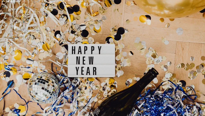 Happy New Year sign with confetti, a small silver disco-like ball, and an open bottle of wine 