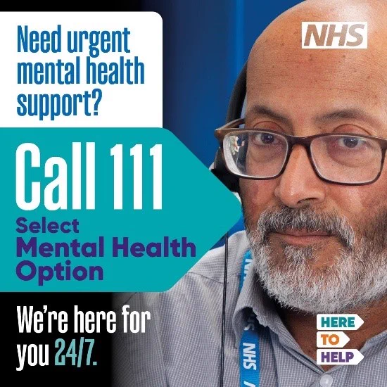 A male NHS worker wearing glasses and a headset with the wording "Need urgent mental health support? Call 111. Select mental health option. We're here for you 24/7. Here to Help."