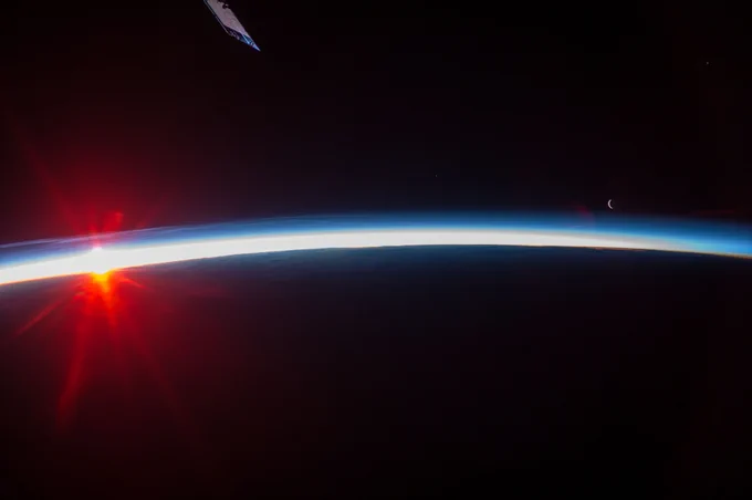 A sunset over the Aleutian Islands,with noctilucent clouds,as documented by the Expedition 36 crew. On the left a red-glowing Sun sets behind Earth's horizon, and to the right the crescent Moon is visible. Credit: NASA