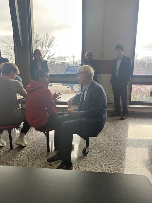 Gov. Evers sits at a table to talk to a student. 