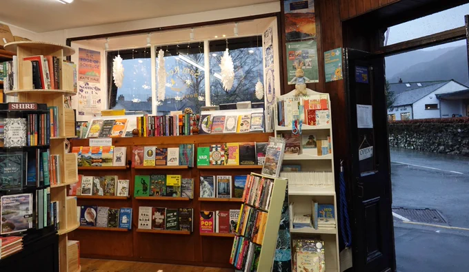 A view of the bookshop looking out onto College Street. The doors are open and the grey outline of Silver Howe is visible above the gallery across the road. Paper snowflakes hang in the bookshop window. 