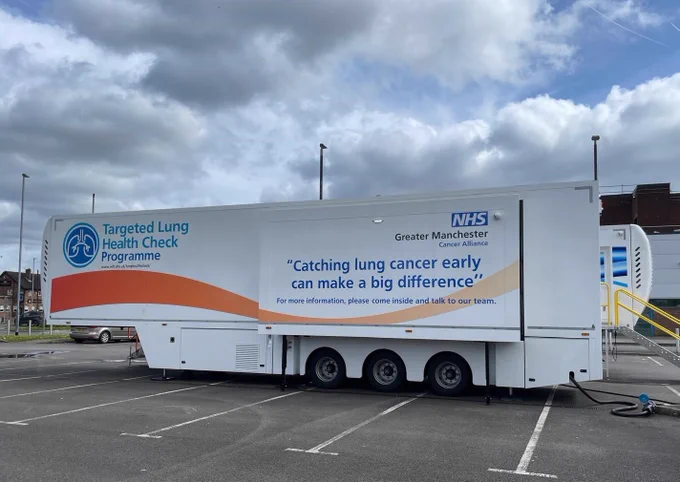 A mobile clinic parked in a car park with the words: Targeted Lung Health Check Programme. “Catching lung cancer early can make a big difference’. 