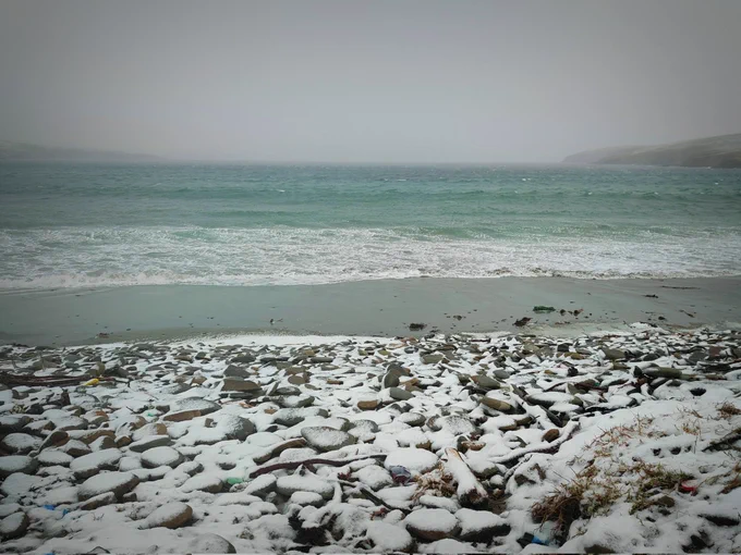 Image shows sea with white waves and snow on rocks
