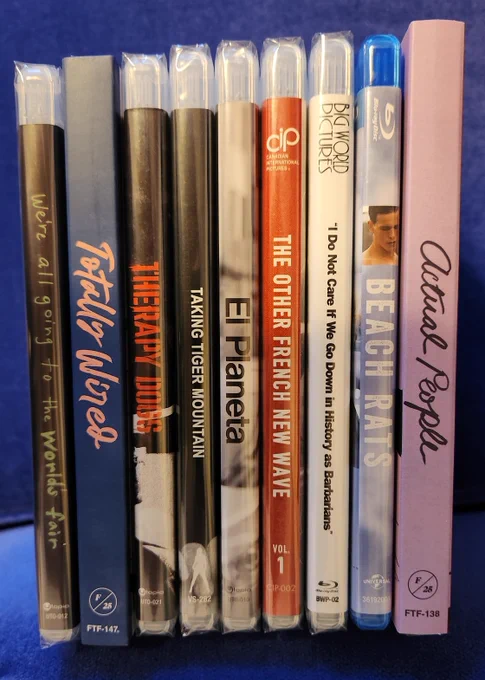 stack of Blu-ray case spines in reverse alphabetical order: WE'RE ALL GOING TO THE WORLD'S FAIR, "Totally Wired": Three Films by Nathan Silver, THERAPY DOGS, TAKING TIGER MOUNTAIN, EL PLANETA, The Other French New Wave Vol. 1, I DO NOT CARE IF WE GO DOWN IN HISTORY AS BARBARIANS, BEACH RATS, and ACTUAL PEOPLE