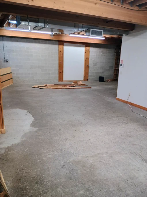 A large, empty gray room with a pile of boards on the ground.