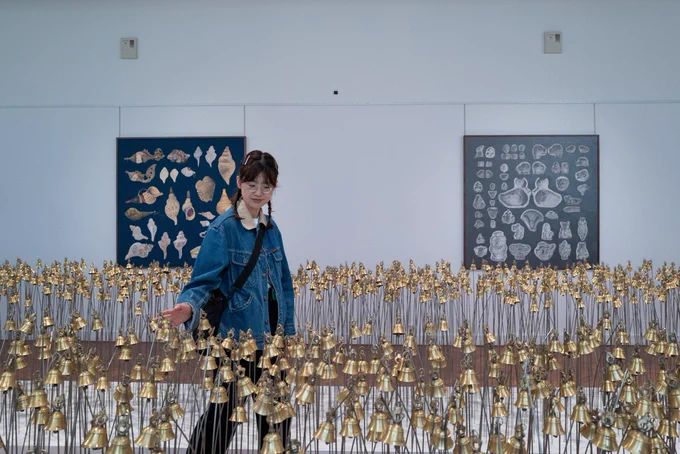 an installation of brass bells and steel rods. Someone is interacting with the bells by brushing them with their hands.